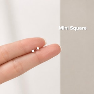 Puede incluir: Un par de diminutos pendientes de botón cuadrados en tono plateado. Los pendientes son pequeños, planos y presentan una forma geométrica sencilla. El texto 'Mini Square' es visible en la esquina superior derecha de la imagen.