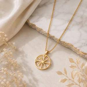 May include: A gold-toned necklace featuring a circular pendant with a cut-out geometric design. The pendant is suspended from a delicate gold-toned chain. The design consists of a central vertical line intersected by diagonal lines and small triangles.