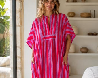 May include: A floor-length kaftan dress featuring vertical stripes in alternating shades of bright pink and light purple. The garment has short, wide sleeves, a split V-neckline with a rectangular panel detail, and side pockets.