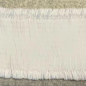 May include: A white fabric trim with a gathered, pleated design. The trim has a raw edge and is ready to be sewn onto a garment or project.