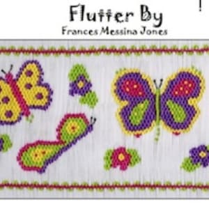 Op de afbeelding: Een witte stof met een kleurrijk geborduurd ontwerp van vlinders en bloemen. De tekst "Flutter By" en "Frances Messina Jones" is op de stof gedrukt.