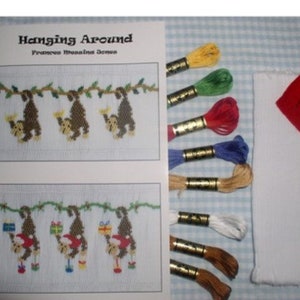 May include: A cross-stitch embroidery pattern titled "Hanging Around" featuring monkeys hanging from a vine. The pattern includes floss in red, blue, green, yellow, white, and brown. The pattern is printed on white paper with a blue and white checkered background.
