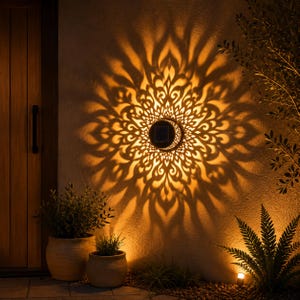 Op de afbeelding: Een ronde wandlamp op zonne-energie gemonteerd op een gestructureerd oppervlak, die een warme amberkleurige gloed uitstraalt en een ingewikkeld, symmetrisch bloemmotief van licht en schaduw op de muur werpt voor een decoratief lichteffect.