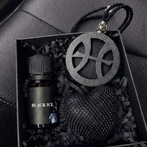 Pode incluir: Uma caixa de presente preta contendo um pequeno frasco de vidro com o rótulo BLACK ICE, um pingente circular preto com um design de basquete recortado em um cordão preto e um objeto preto texturizado em forma de coração.