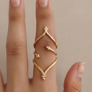 May include: A gold-toned ring featuring a multi-layered, open-ended design that wraps around the finger. The ring consists of two chevron-shaped bands connected by a spiral element, with each terminal point accented by a small cluster of three beads.