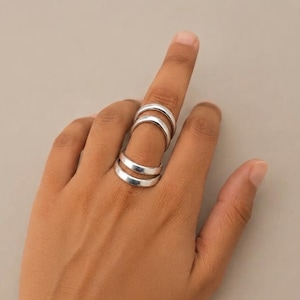 Peut inclure: Un ensemble de deux bagues en argent lisse et poli portées sur un seul doigt. Les bagues présentent un design simple à anneau arrondi avec une finition métallique réfléchissante, positionnées l'une au-dessus de l'autre sur le doigt.
