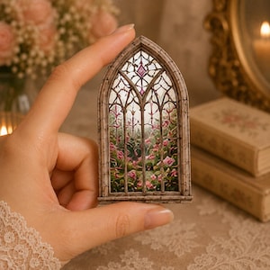 May include: A miniature arched window frame featuring a detailed stained glass design with intricate leaded patterns. The glass depicts a lush garden scene filled with pink roses and green foliage, accented by small purple diamond-shaped glass panes.