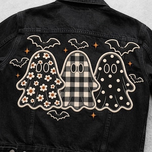 May include: A black denim jacket featuring an embroidered design on the back. The embroidery depicts three ghosts with different patterns: one with white daisies, one with a black and white plaid check, and one with white polka dots, surrounded by bats and stars.
