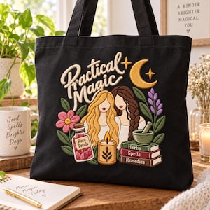 Op de afbeelding: Een zwarte canvas tas met een geborduurd ontwerp met de tekst "Practical Magic" boven twee figuren met lang haar. Het borduurwerk bevat een gele halve maan, een roze bloem, een potje met het label "Rose Petals", een brandende kaars en een stapel boeken met de labels "Herbs", "Spells" en "Remedies" met een vijzel.