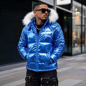 Puede incluir: Una chaqueta acolchada de color azul metálico brillante con capucha ribeteada en piel sintética blanca, cremallera frontal completa y el texto "VENGEANCE78" impreso en blanco en el pecho izquierdo. La prenda presenta un diseño acolchado.