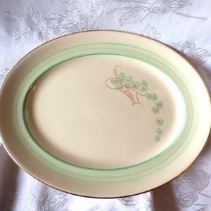 May include: Oval serving platter with a cream-coloured centre and a light green border. The rim is trimmed with gold. A floral basket design is on the left side of the platter.