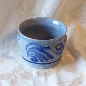 May include: A small blue and white ceramic pot with two handles. The pot has a textured surface and a blue and white design.