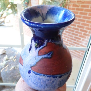 May include: A small blue and white ceramic vase with a pink glaze and a brown and blue design. The vase is hand-painted and has a unique, rustic look.