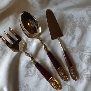 May include: A set of three silver-toned serving utensils with dark brown wooden handles. The utensils include a fork, a spoon, and a small knife.