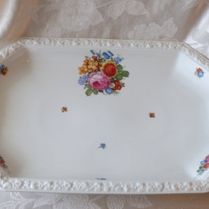 May include: White octagonal serving platter with a raised rim and a floral design in the centre. The design features a bouquet of pink, red, yellow, and blue flowers.