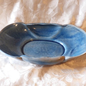 May include: A blue ceramic bowl with a wavy rim and a smooth, glazed interior. The bowl is oval-shaped and has a slightly raised centre.