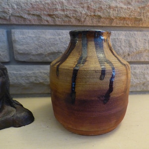 Peut inclure: Un vase en céramique brun avec un glaçage coulant noir et brun. Le vase a un corps arrondi et une ouverture légèrement évasée.