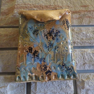 May include: A ceramic wall pocket with a blue and brown floral design. The pocket has a textured surface and a scalloped edge.
