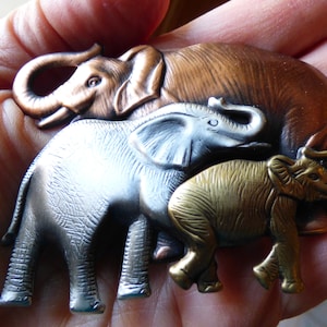 May include: A set of three metal elephant figurines, each with a different color and texture. The largest elephant is copper, the middle elephant is silver, and the smallest elephant is gold.