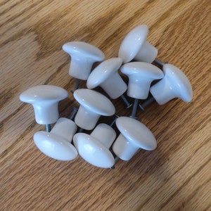 May include: A group of 12 white ceramic cabinet knobs with silver screws.