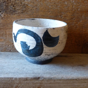 May include: A ceramic bowl with a white base and dark blue abstract design. The bowl has a rounded shape with a slightly flared rim and a dark blue base. The bowl is sitting on a wooden surface.