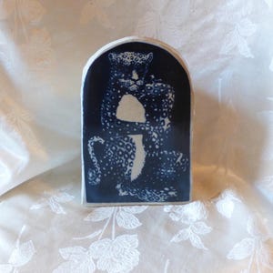 May include: A ceramic decorative piece featuring a navy blue leopard design against a white background. The leopard is depicted in a stylized, artistic manner, with a dark blue arch shape. The piece is likely handmade and suitable for home decor.