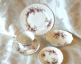 May include: A white porcelain tea set with a floral rose pattern and gold trim. The set includes a teacup and saucer, a dinner plate, a small oval dish, and a small round dish.