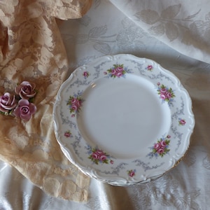 May include: A set of four white ceramic dinner plates with a delicate floral design featuring pink and blue roses. The plates have a scalloped edge and a gray floral pattern.