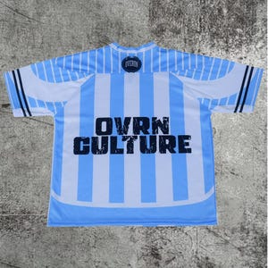 May include: A short-sleeve jersey featuring vertical light blue and white stripes. The text OVRN CULTURE is printed in large, distressed black letters across the center. A small circular logo with the word OVERON is positioned at the neckline.