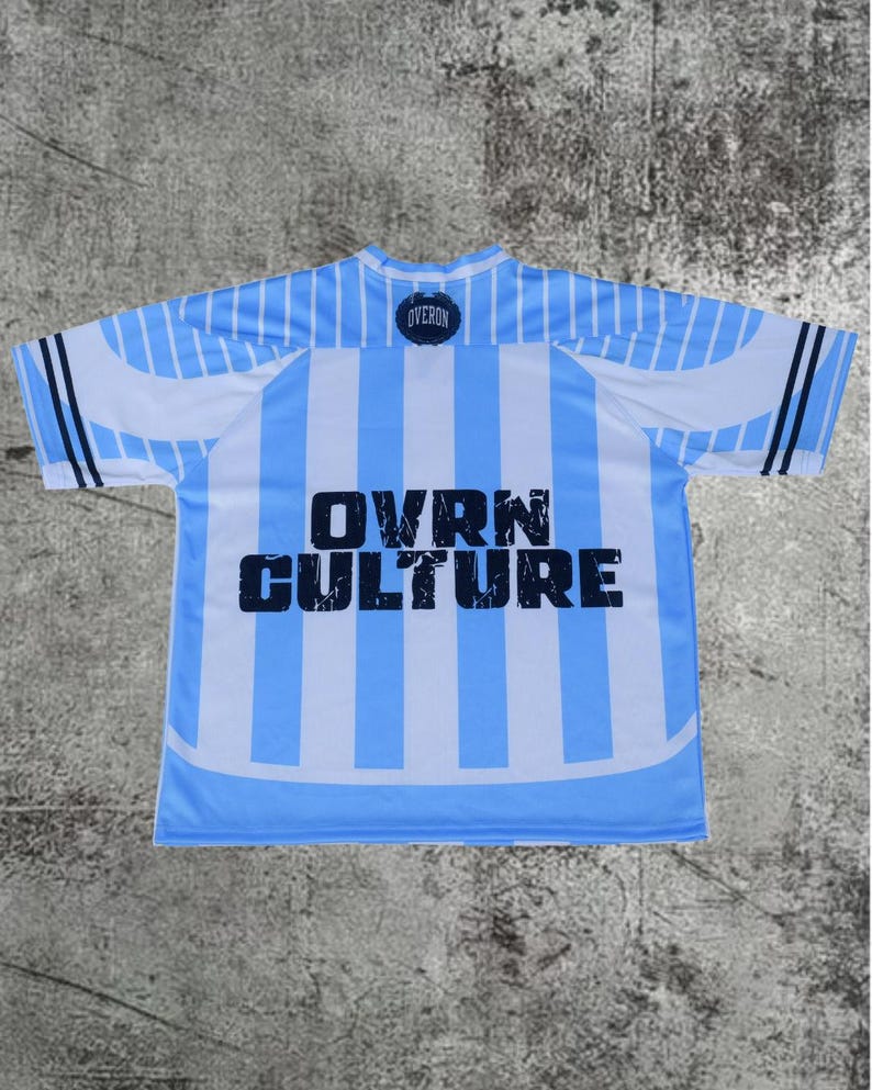 May include: A short-sleeve jersey featuring vertical light blue and white stripes. The text OVRN CULTURE is printed in large, distressed black letters across the center. A small circular logo with the word OVERON is positioned at the neckline.