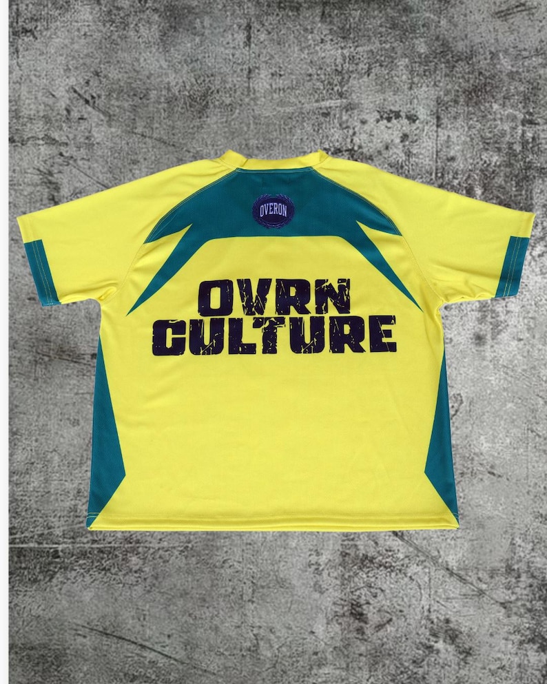 May include: A short-sleeve t-shirt in bright yellow with dark teal accents on the shoulders and sides. The back features a dark purple circular logo with the text OVERON and the large, distressed dark purple text OVRN CULTURE printed below.
