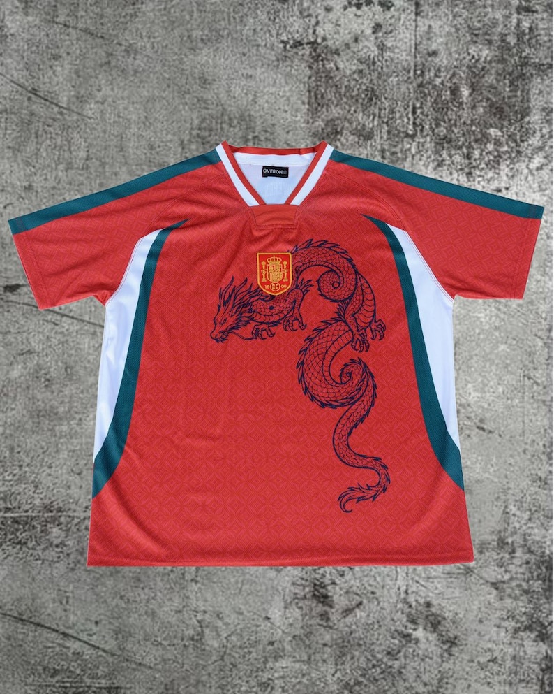 May include: A red short-sleeve jersey featuring a dark blue dragon graphic on the front, a yellow and red crest emblem, and white and dark green side panels. The collar is white with red trim, and the interior label displays the text OVERON.