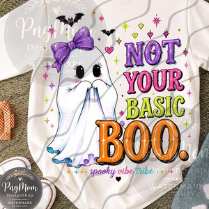 May include: A white long-sleeve sweatshirt featuring a graphic of a ghost wearing a purple bow, surrounded by small bats, stars, and hearts. The text reads NOT YOUR BASIC BOO in purple, pink, green, and orange, with spooky vibe tribe below.