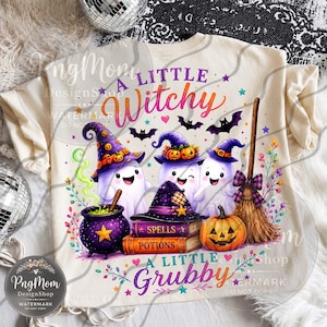 Op de afbeelding: Een crèmekleurig t-shirt met een grafische print van drie witte geesten met paarse heksenhoeden, een paarse ketel, een stapel boeken met het label Spells en Potions, een pompoen en een bezem, met de tekst A LITTLE Witchy A LITTLE Grubby.