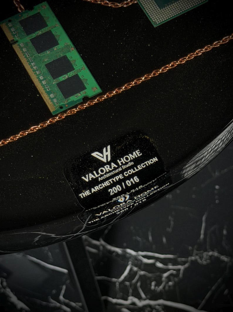 May include: A black circular surface featuring a green RAM stick and a copper-colored chain. A black label displays the text: VALORA HOME, Architectural Studio, THE ARCHETYPE COLLECTION, 200 / 016. The base has a black and white marble pattern.