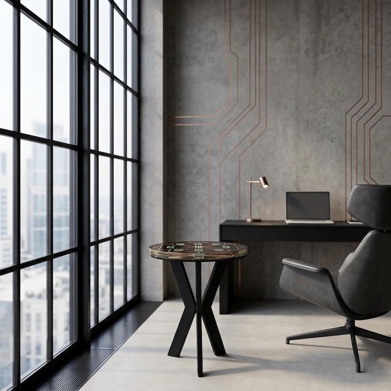 May include: A round side table with a dark patterned top and a black metal base featuring four intersecting legs. The table is positioned in a room with a large window, a black desk with a laptop, a desk lamp, and a dark gray swivel chair.
