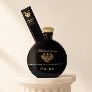 May include: A round black glass fragrance diffuser bottle with a gold cap, featuring the text Noblesse d'Arôme and Nuit D'Or in gold lettering. A black rectangular box labeled Fragrance Sticks is positioned behind the bottle.