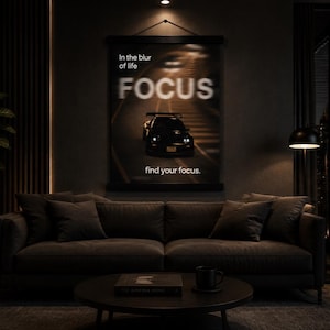 Puede incluir: Un póster rectangular para colgar en la pared con un coche deportivo negro en una carretera borrosa. El texto dice In the blur of life FOCUS find your focus. El póster está montado con listones de madera negra arriba y abajo.