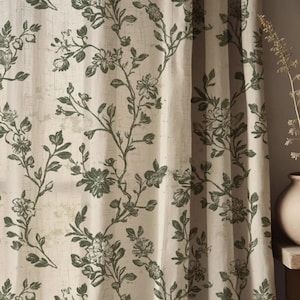 May include: A light beige curtain featuring a repeating dark green botanical print of climbing vines, leaves, and flowers. The fabric has a visible woven texture, and the curtain hangs in soft vertical folds, allowing light to filter through.
