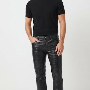 Könnte beinhalten: Ein schwarzes kurzärmeliges T-Shirt mit Rundhalsausschnitt kombiniert mit einer schwarzen Hose mit texturiertem Krokodilprägemuster. Die Hose hat ein klassisches Fünf-Taschen-Design mit Knopfverschluss und wird mit schlichten weißen Sneakern getragen.