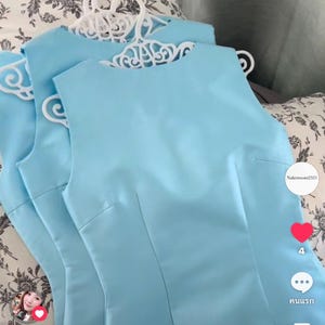 Puede incluir: Dos vestidos sin mangas de color azul claro con cuello redondo y detalles de costuras verticales en la parte delantera. Cada vestido cuelga de una percha de plástico blanca con un diseño recortado intrincado en la parte superior.