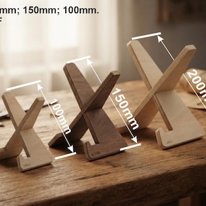 Peut inclure: Trois supports en bois en forme de X dans des tons marron clair et moyen, étiquetés Small, Medium et Large. Les supports présentent des dimensions de 100mm, 150mm et 200mm, indiquées par des lignes de mesure et du texte sur l'image.