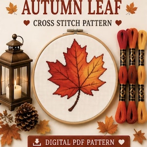 May include: A cross stitch pattern featuring an autumn maple leaf in shades of red, orange, and yellow inside a wooden embroidery hoop. Beside it are three skeins of embroidery floss in matching colours, a lantern with a candle, and a pinecone.