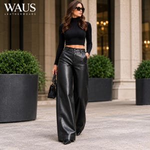 Pode incluir: Um top curto preto de manga comprida com gola alta combinado com calças largas de couro preto de cintura alta. O conjunto inclui uma pequena mala preta e óculos de sol escuros. O texto WAUS LEATHERWEARS é visível no canto superior esquerdo.