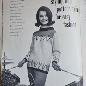 May include: A vintage advertisement features a woman wearing a white sweater with blue and black geometric patterns. The sweater has a high neck and long sleeves. The text reads "Youthful styling and pattern trims for easy fashion."