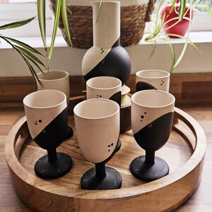 Peut inclure: Un ensemble de six verres à boire en céramique noir et blanc avec un design minimaliste, disposés sur un plateau en bois avec un pichet en céramique assorti.