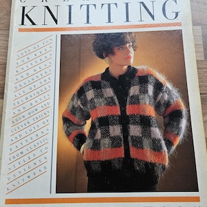 Op de afbeelding: Een vintage boek getiteld "Creative Knitting" van Pam Dawson. De omslag toont een vrouw in een zwart, oranje en grijs geruit vest. De titel van het boek staat in grote letters, met extra tekst die de inhoud beschrijft.
