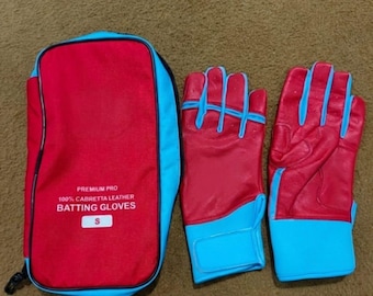Könnte beinhalten: Ein Paar rote und hellblaue Schlaghandschuhe neben einer passenden roten und hellblauen Aufbewahrungstasche. Die Tasche trägt den Text PREMIUM PRO 100% CABRETTA LEATHER BATTING GLOVES und ein weißes Etikett mit dem Buchstaben S.