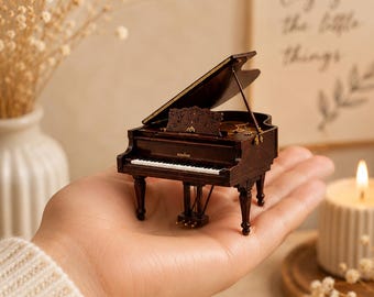 Puede incluir: Un piano de cola en miniatura de madera marrón oscuro con acabado pulido, un teclado detallado con teclas blancas y negras, un atril con intrincados patrones recortados, tres pedales y una tapa abierta que revela la estructura interna.