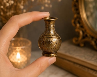 Peut inclure: Un vase miniature en laiton avec un col étroit et un corps arrondi, présentant des motifs floraux et géométriques gravés sur toute sa surface métallique. Le petit récipient possède un bord évasé et une base circulaire patinée.